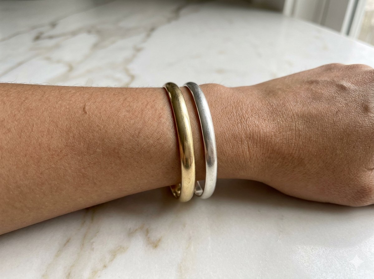 Poignet portant un bracelet doré et un bracelet argenté côte à côte pour comparer leur effet sur la peau