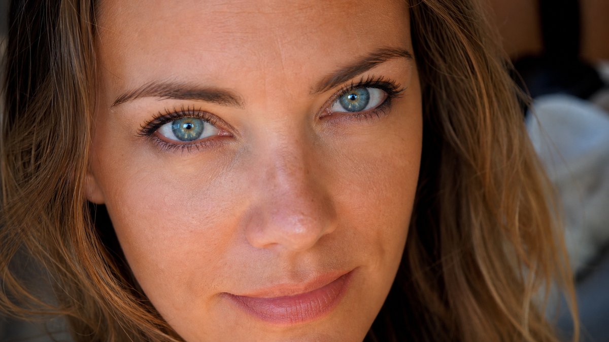 Portrait en gros plan d'une femme aux yeux bleu-vert intenses et aux cheveux châtain doré chaud, teint lumineux